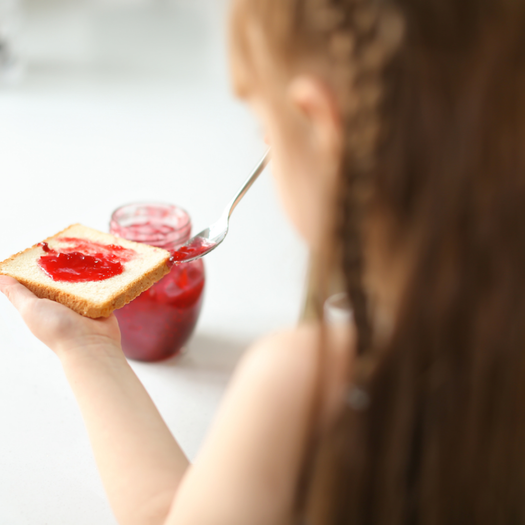 child spreading jam on bread