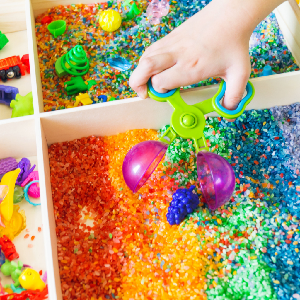 a child using a scooping tool with brightly coloured sand and beads