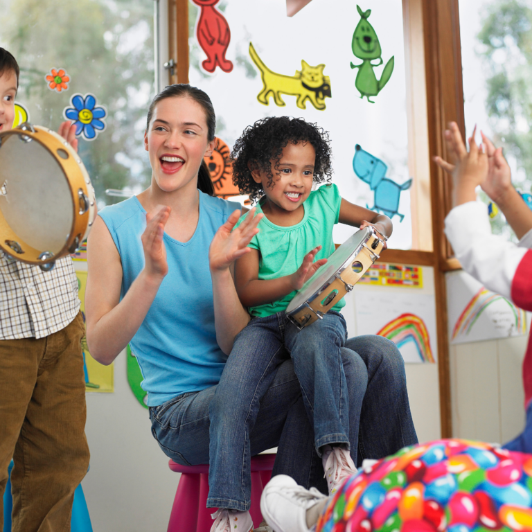 A nursery teacher and some preschool children enjoying making music and dancing together