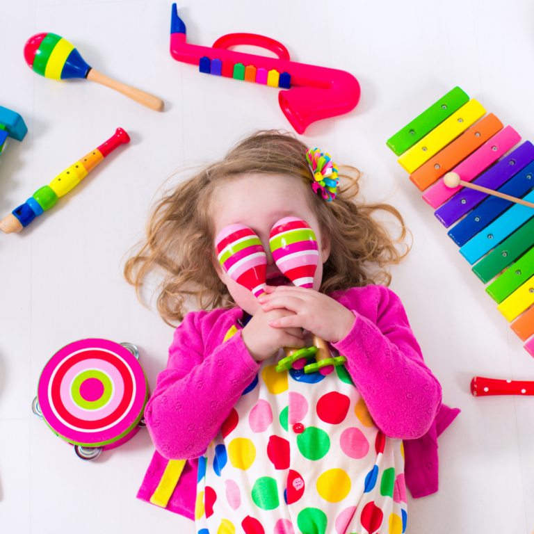 A bright image of a preschool child lying on the floor with a selection of colourful musical instruments.