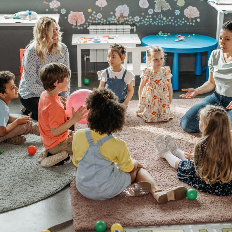 Nursery staff sitting in a circle with children singing and clapping