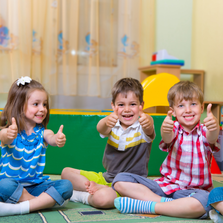 An image of preschool children with their thumbs up and smiling to express positivity.