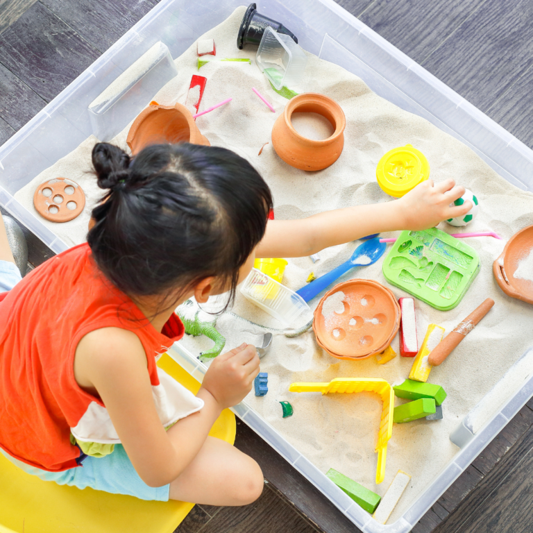 An image of a preschool child exploring a sand and container activity in a tuff tray