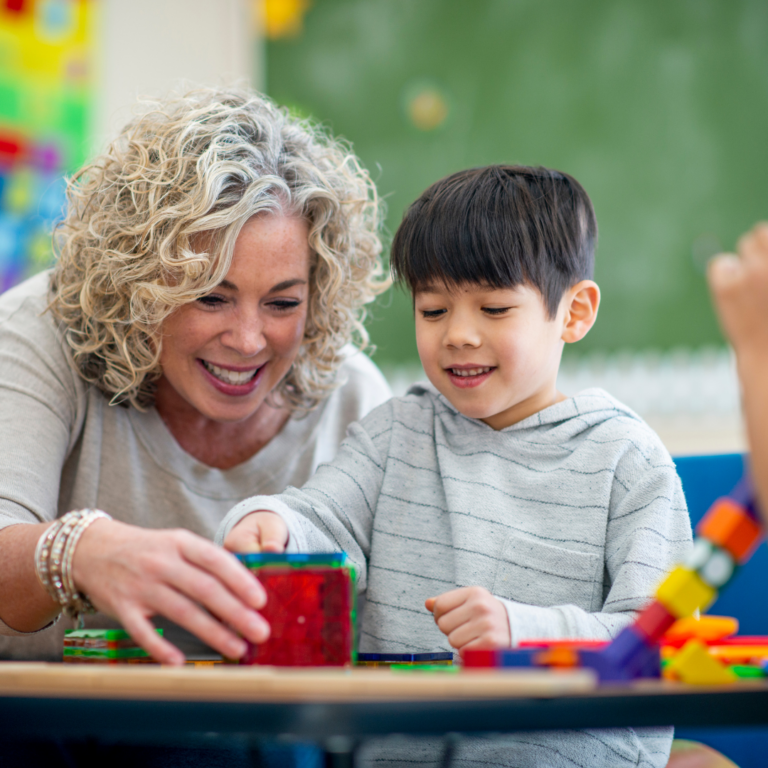 Nursery teacher with a nursery aged child building a tower with blocks