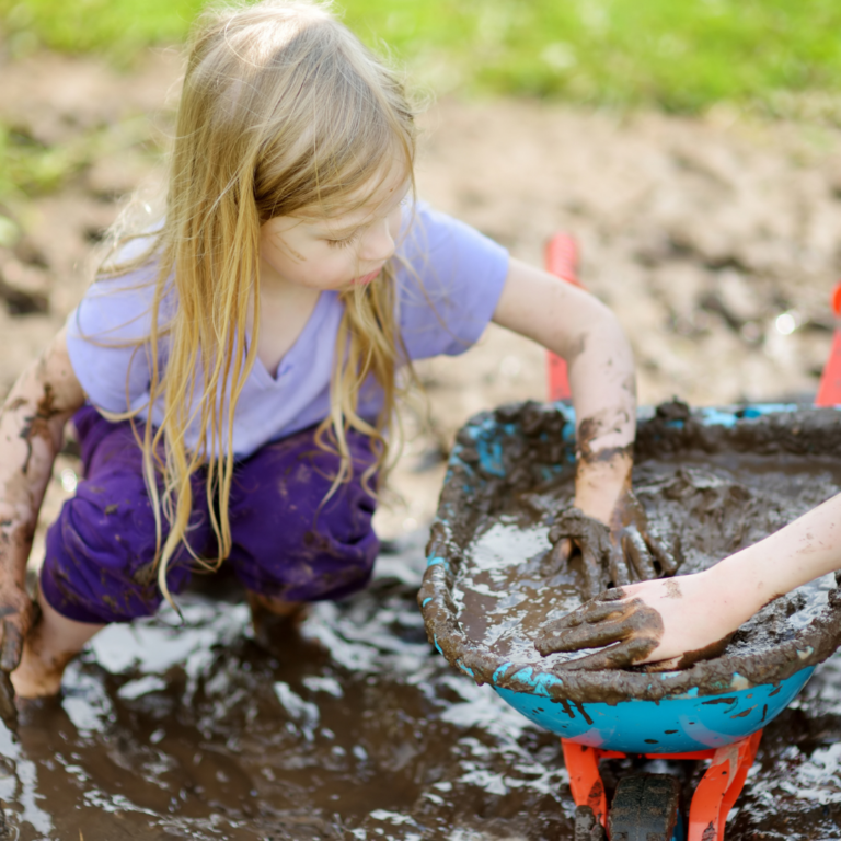 A small child enjoying exploring the mud in the outdoors area of a nursery school.