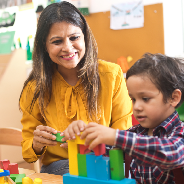 A nursery practitioner supporting and working alongside a child with SEND to complete a construction activity with blocks.